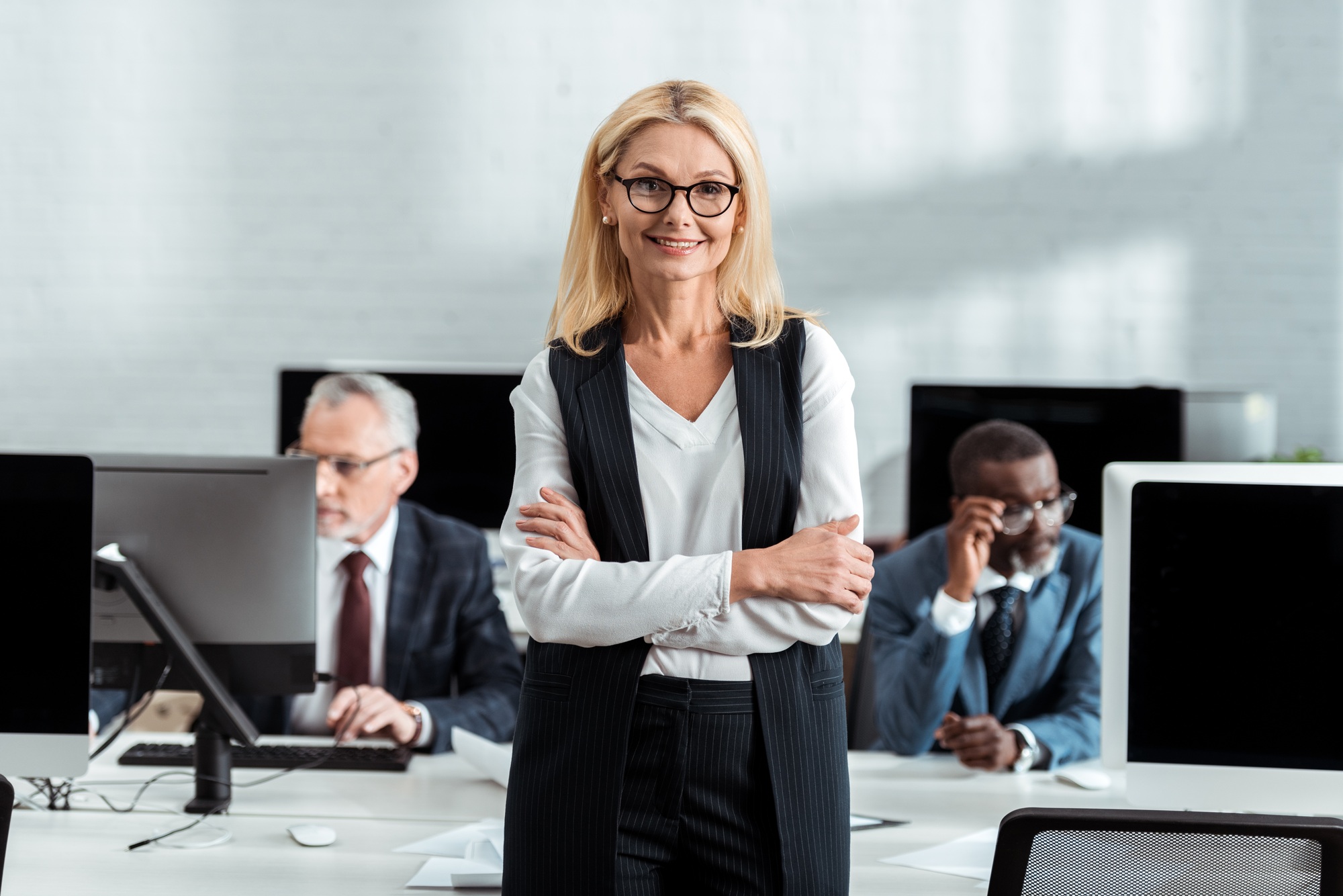 selective focus of cheerful businesswoman standing with crossed arms near multicultural men in