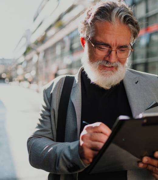 Senior business man standing outside and taking notes on a clipboard Senior business man standing outside and taking notes on a clipboard